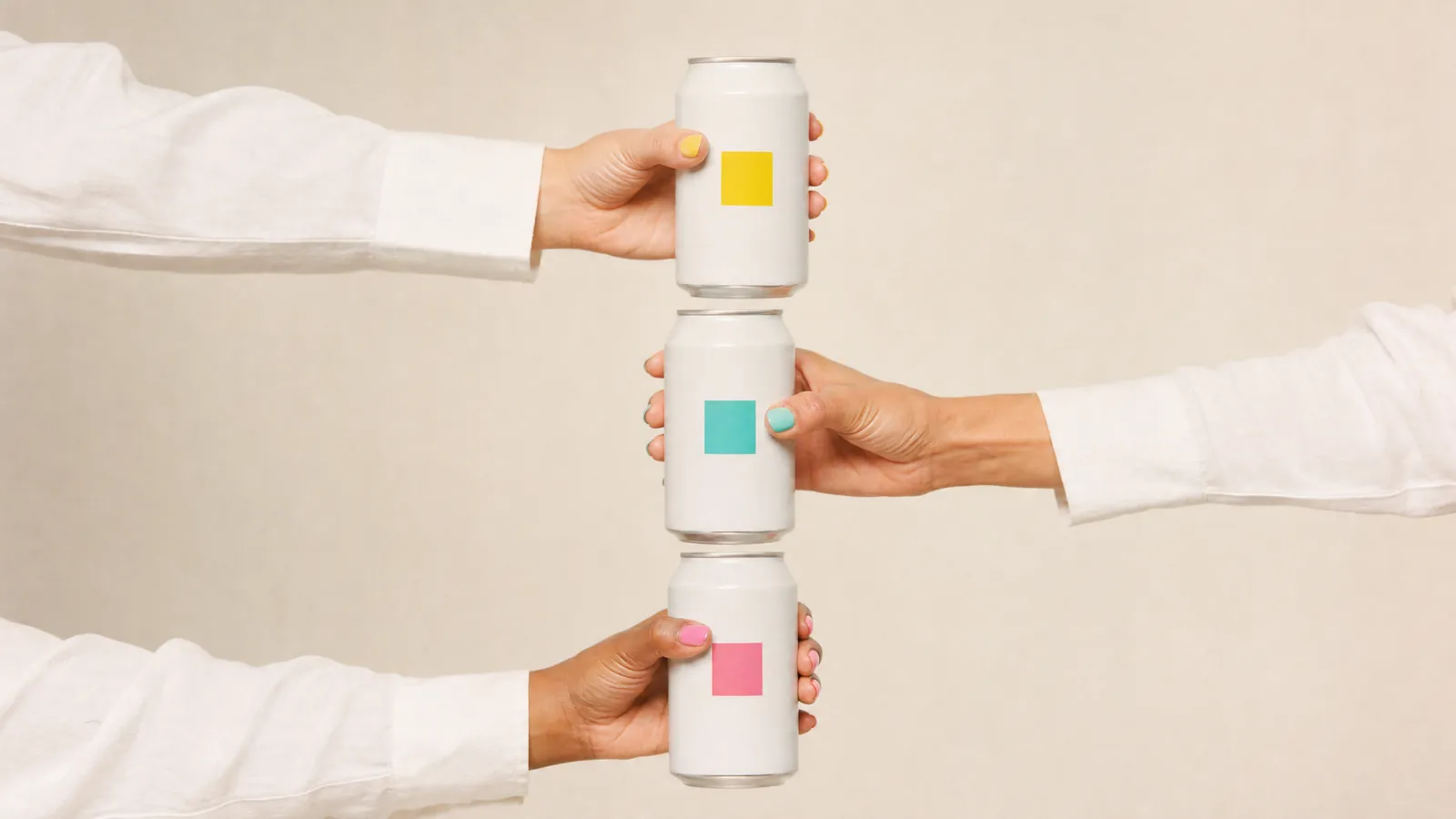 Three hands reaching in from the sides, each holding a plain white can with a square of colour on it, stacked down the middle of the frame