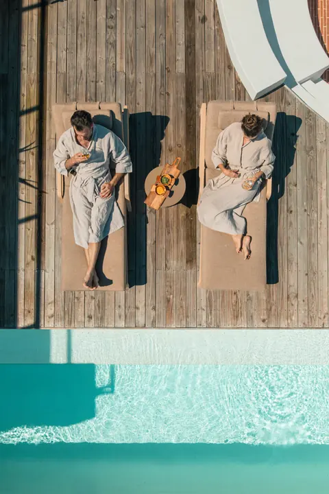 From above, two guests in robes rest on loungers by the pool