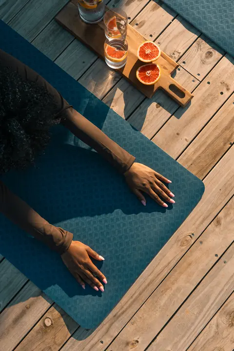 From above, hands on a yoga mat beside a tray of grapefruit and water