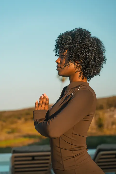 A woman holds a prayer pose, the veld behind her