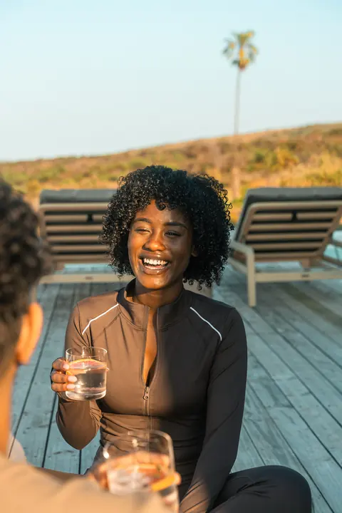 A woman laughs over a glass of water on the pool deck
