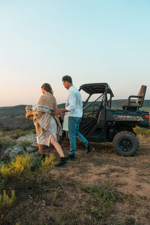A couple walk to the off-road vehicle through the fynbos at dusk