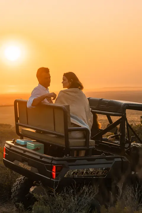A couple sit in the back of the off-road vehicle at sunset