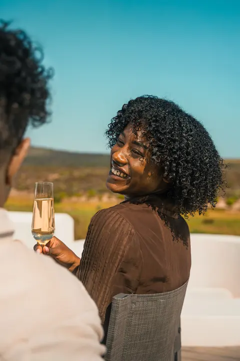 A woman smiles over her shoulder, a glass of sparkling wine in hand