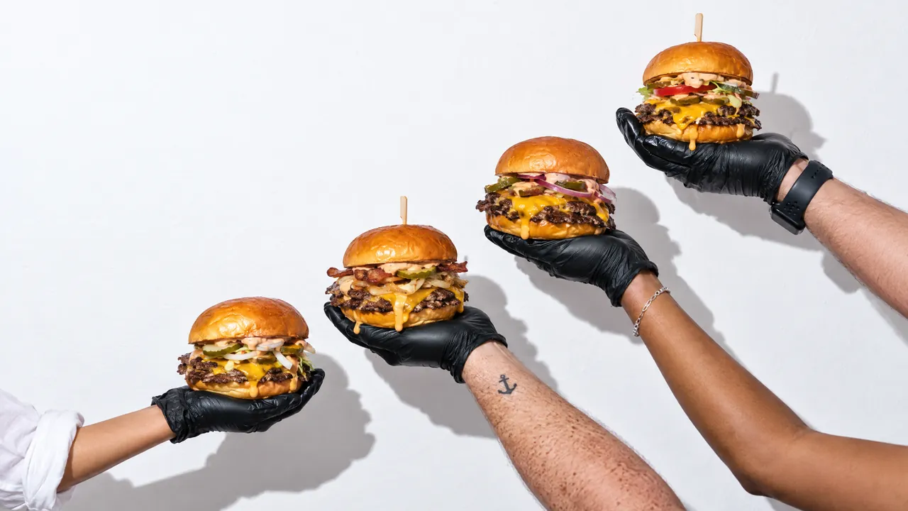 Gloved hands hold four burgers against a white wall, made with AI