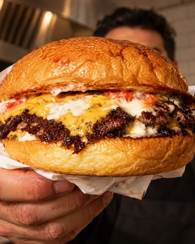 A cook holds a double smash burger out to the camera